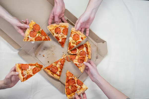 Hands sharing slices of pepperoni pizza — family-style at Roma Pizza Donair