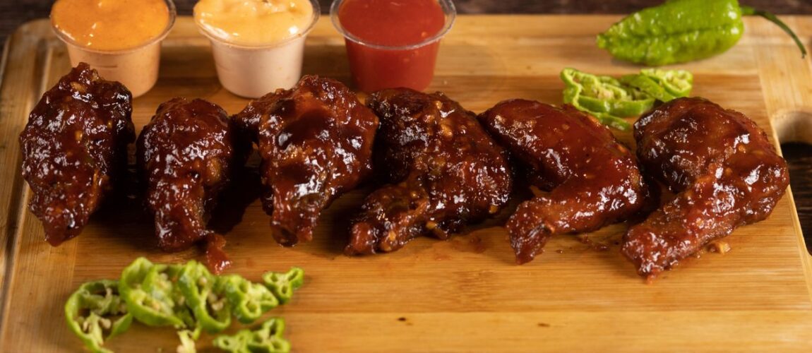 Barbecue chicken wings with dipping sauces on a wooden board at Roma Pizza Donair